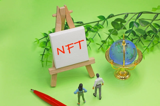 キャンバスに NFT と描かれたミニチュアの絵画と、それを眺める2人の人形